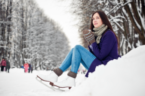 Woman in ice skates sitting in a snow bank with a warm beverage for some reason.